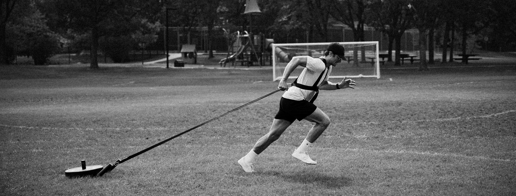 Connor pulling a weighted sled across a grass field