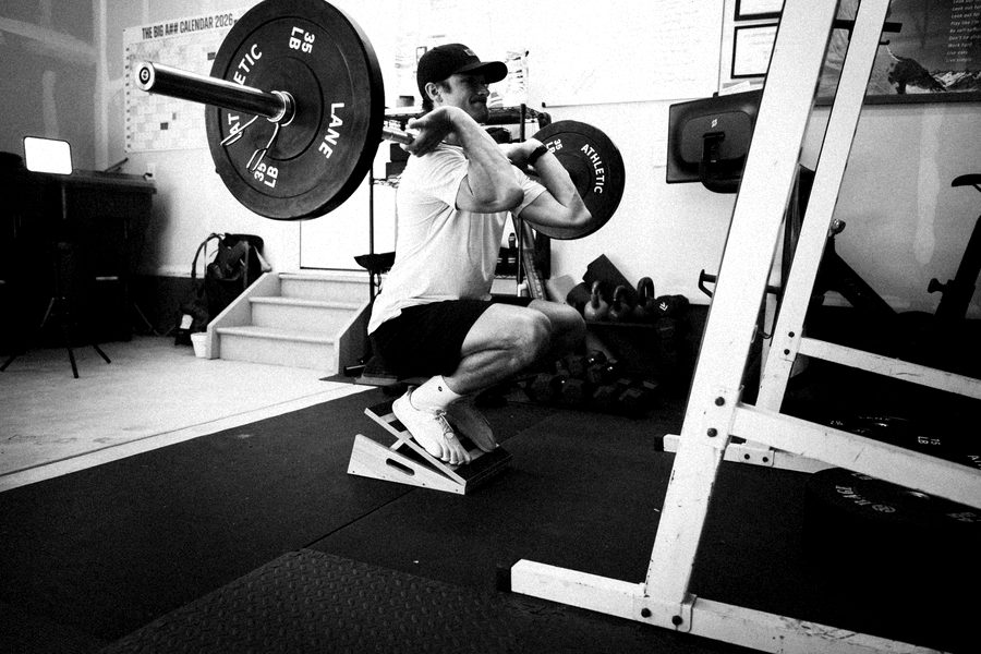 Connor in a barbell front squat on a slant board in his garage gym