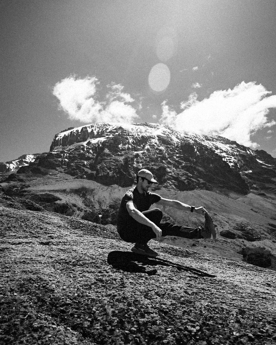 Connor holding a pistol squat on a rock slab on Kilimanjaro, the snow-capped summit behind him