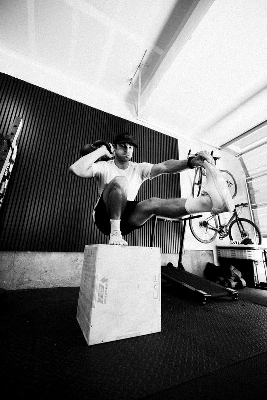 Connor balanced in a pistol squat on top of a plyo box in his garage, holding his free foot out in front
