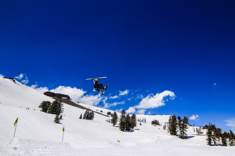 Connor upside down in a cork off a park jump in Tahoe, blue sky and pines behind him