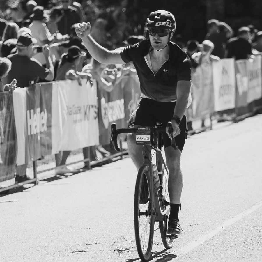 Connor crossing the Gran Fondo finish line on his road bike, fist in the air