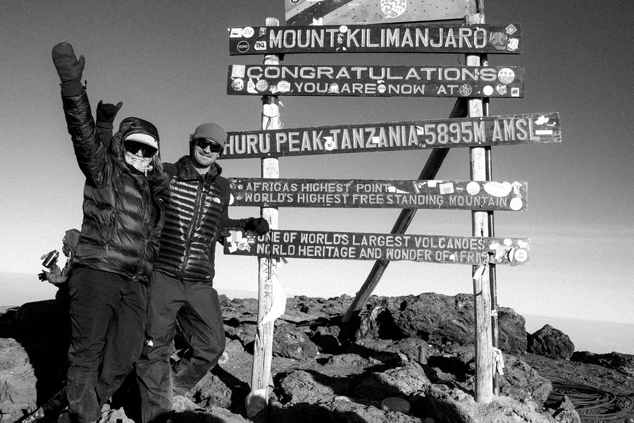 Connor and his partner at the Uhuru Peak summit sign on Kilimanjaro, arms up