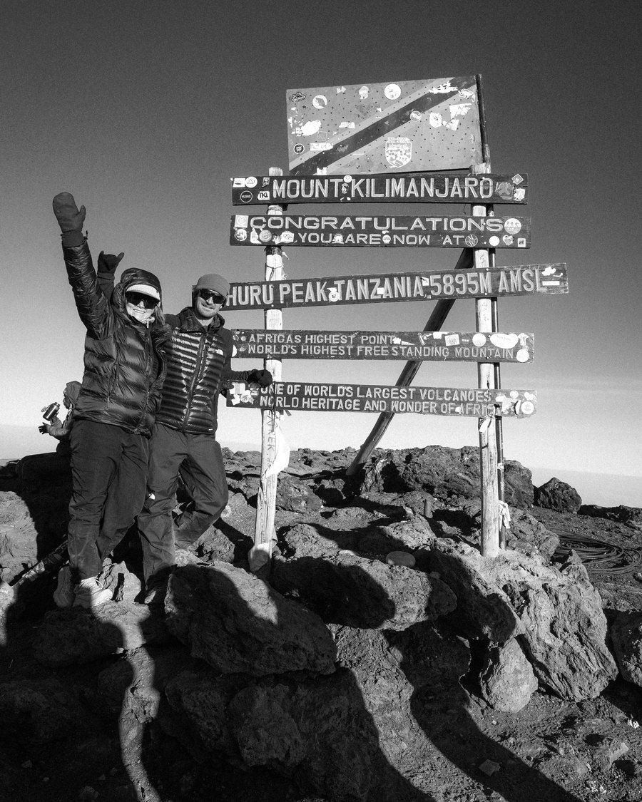 Connor and his partner at the Uhuru Peak summit sign on Kilimanjaro, arms up