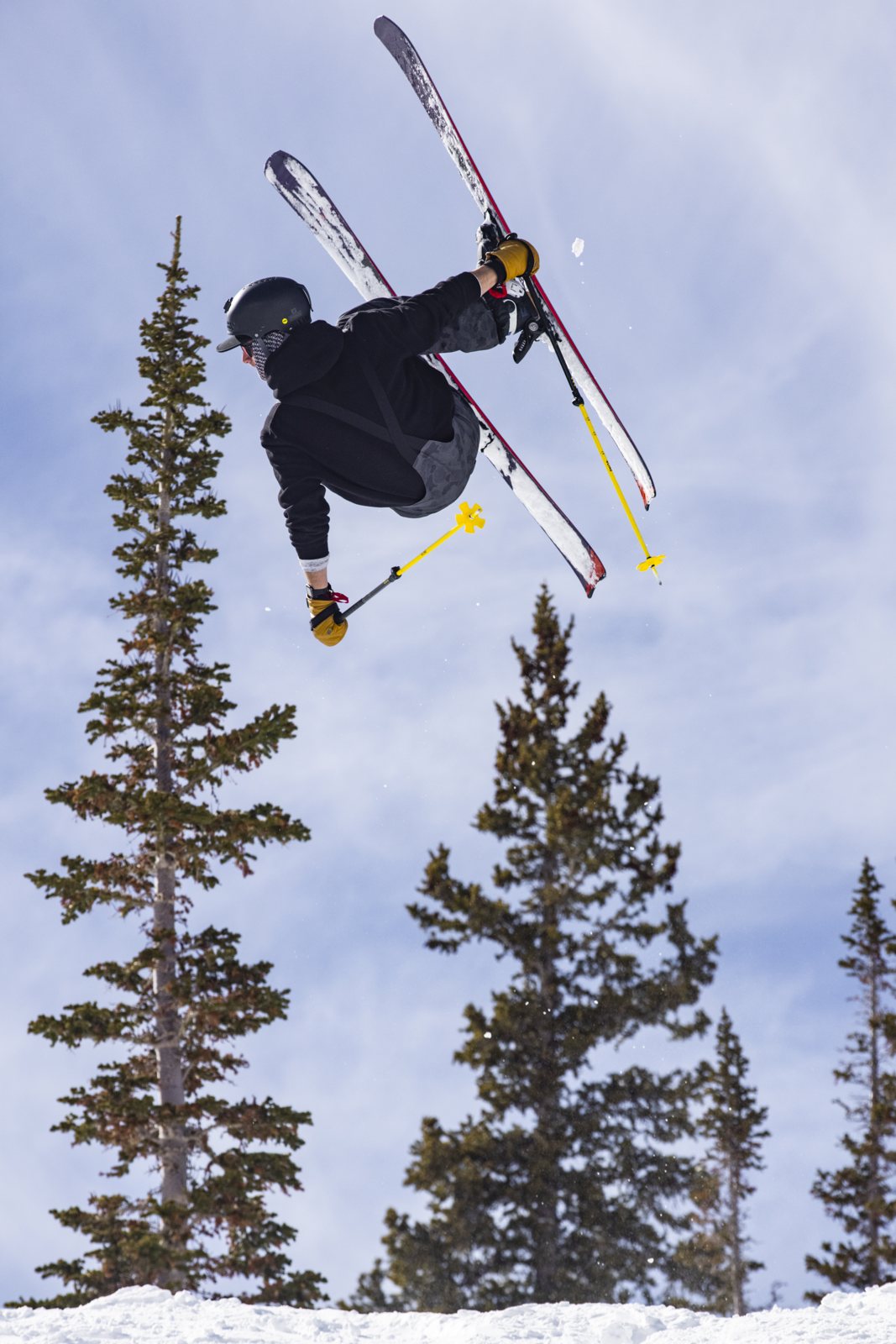 Connor mid air on skis above the trees at Alta