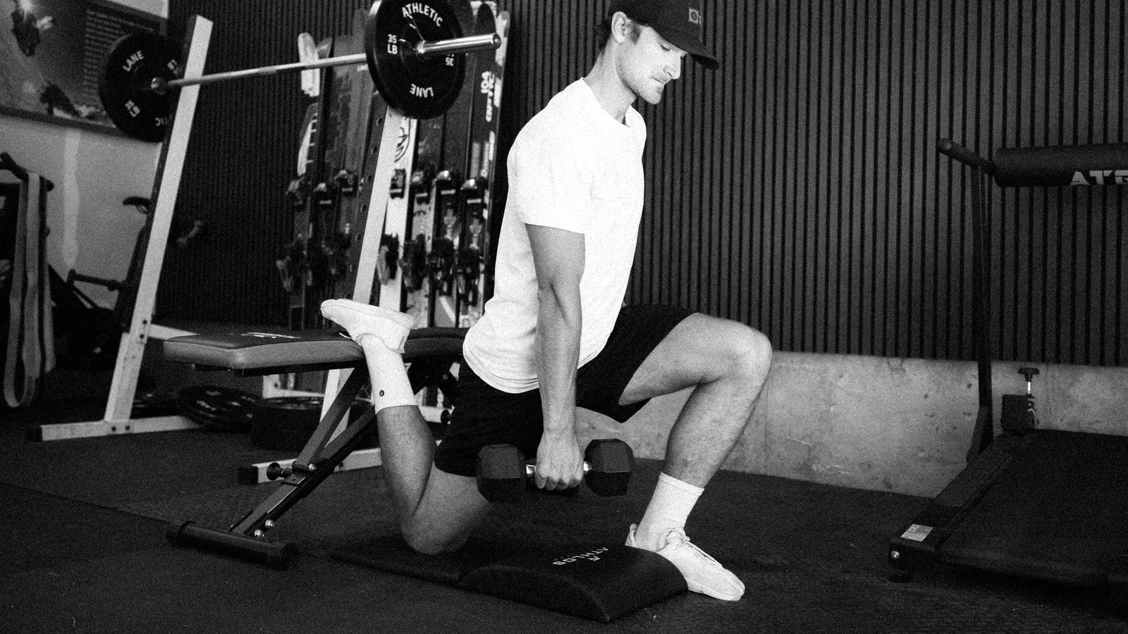 Connor at the bottom of a loaded split squat in his garage gym, dumbbells at his sides
