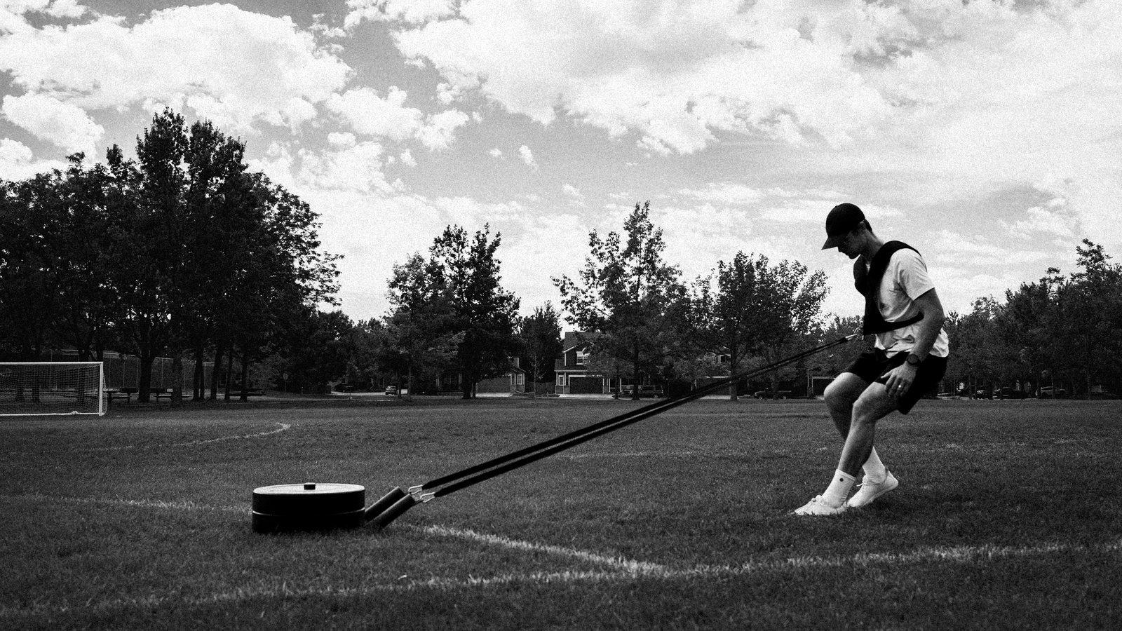 Connor dragging a weighted sled backward across a grass field